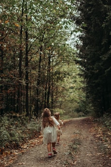 a couple of children walking on a path in the woods