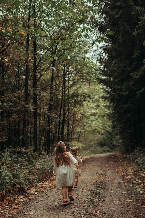 a couple of children walking on a path in the woods