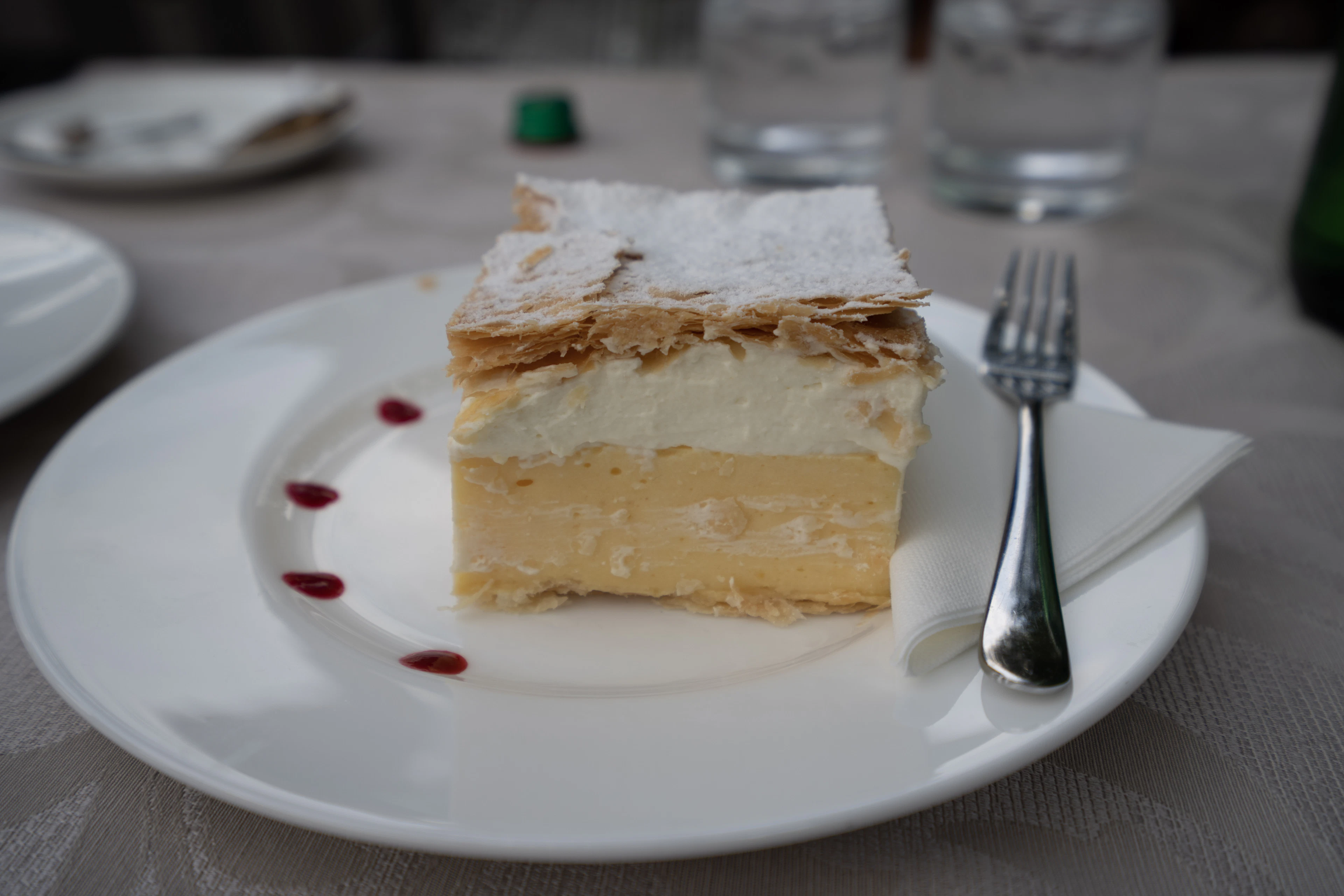 A slice of custard cream cake dusted with icing sugar, served on a restaurant plate at Lake Bled, Slovenia
