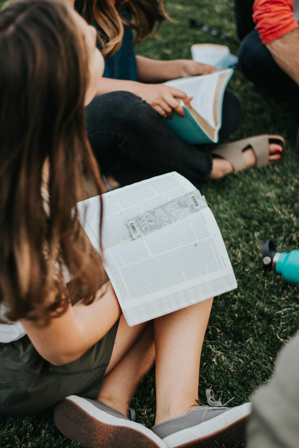 a group of people sitting on the grass reading a book