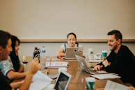 a group of people sitting at a table with laptops