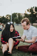 a man and woman sitting on grass looking at a tablet