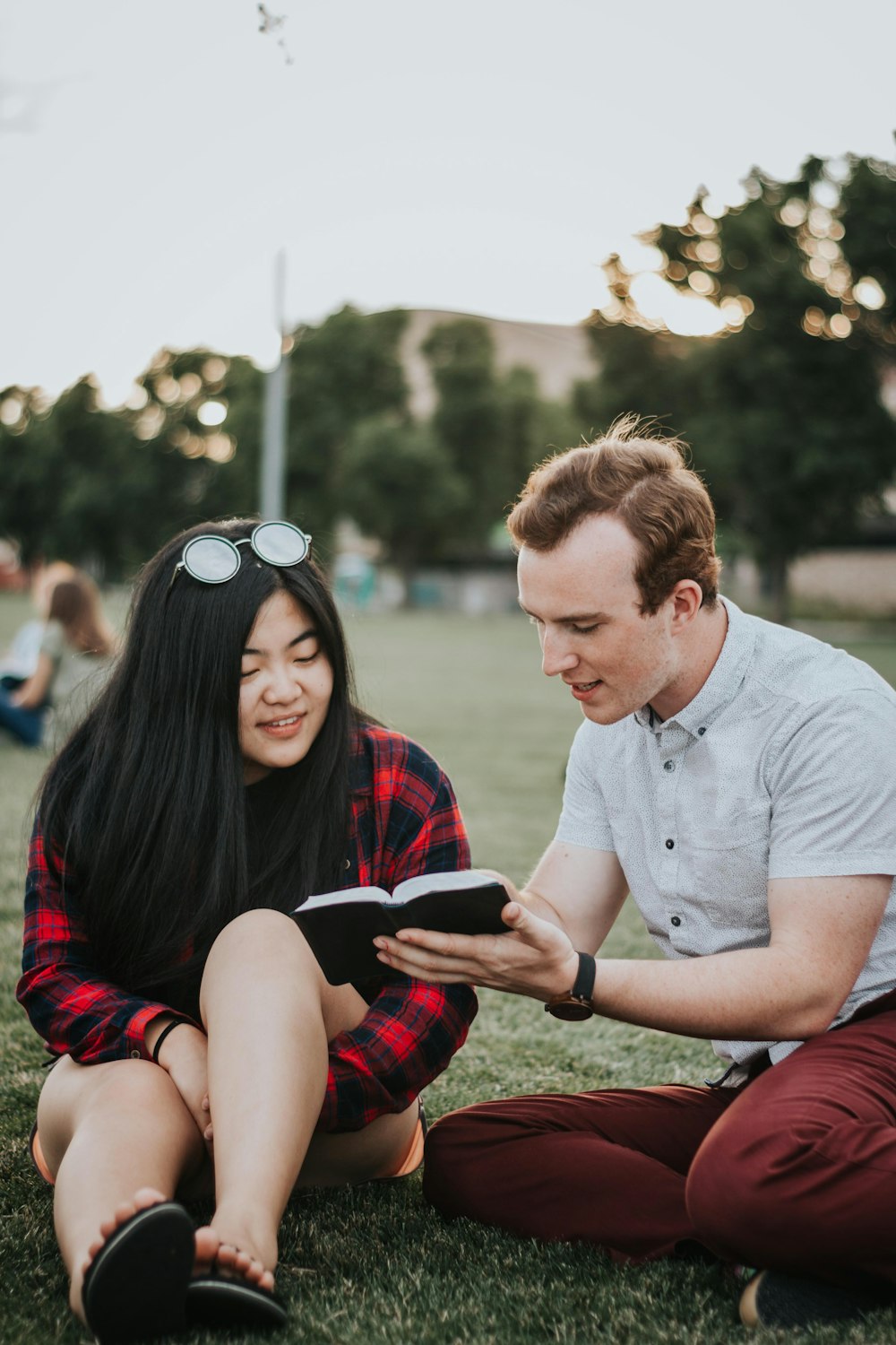 a man and woman sitting on grass looking at a tablet