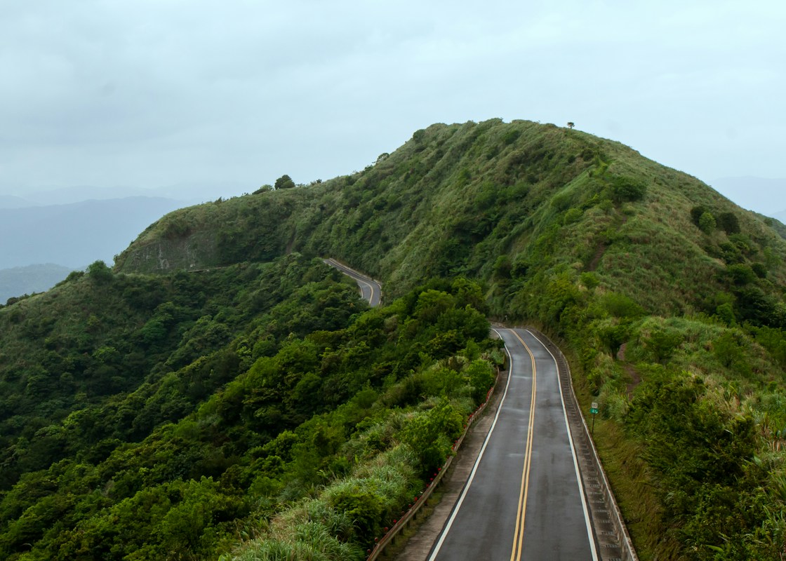 台灣山區蜿蜒的雙線道公路，兩旁是綠色山坡