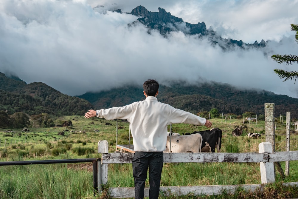 a man standing in front of a fence looking at cows