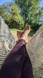 Relaxing in a hammock with crossed legs, surrounded by a lush green garden. Sunlight filters through the leaves, creating dappled shadows on the ground.