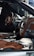 The interior of a luxury car features brown leather seats, a modern ergonomic steering wheel, and a sophisticated dashboard with advanced controls. A racing helmet is placed on the passenger seat beside the gear shift.