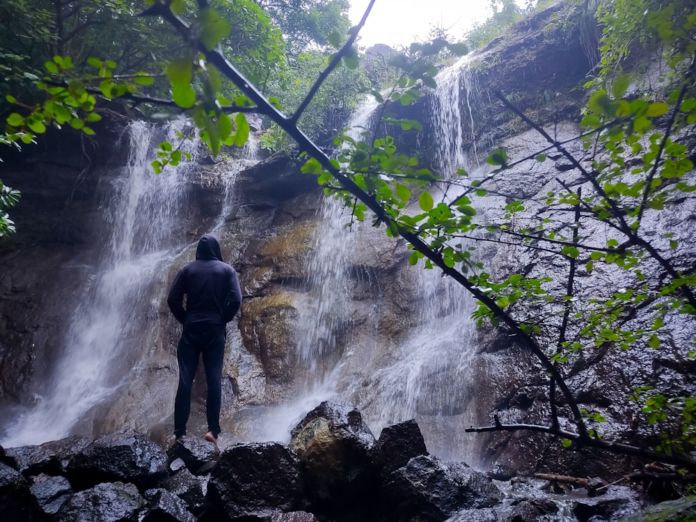 a person standing on a rocky ledge looking at a waterfall