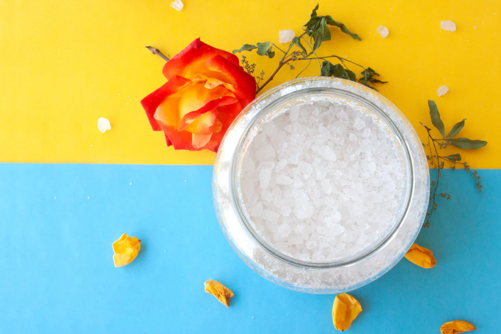 Metal bowl of bath salt beside a rose
