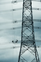 Construction workers building a high-tension power line tower in a rural area.