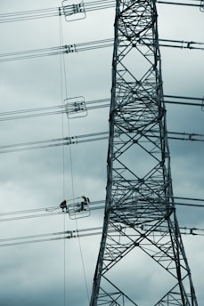 Construction workers building a high-tension power line tower in a rural area.