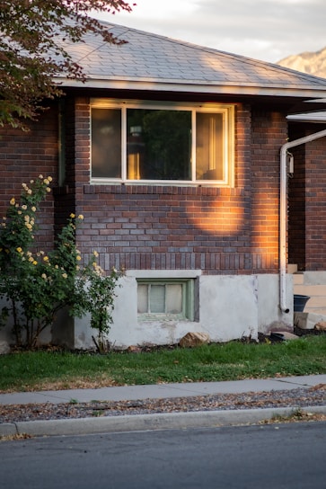 A friendly home inspector carefully examining a house's foundation with tools in hand on a sunny day.