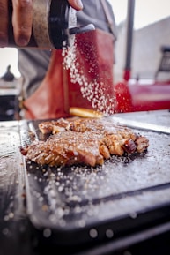 Close-up of a chef expertly seasoning a thick cut of beef over an open flame.