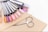 A collection of nail polish color samples displayed on nail swatches fan out over a beige surface. Nearby, a wooden cuticle stick and a small pair of nail scissors are placed. The color samples range from pastels to vibrant hues.