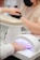 A person is receiving a manicure, with the focus on their hand under a UV nail lamp. Another person wearing a mask is performing the manicure. A beige armrest is visible next to the lamp.