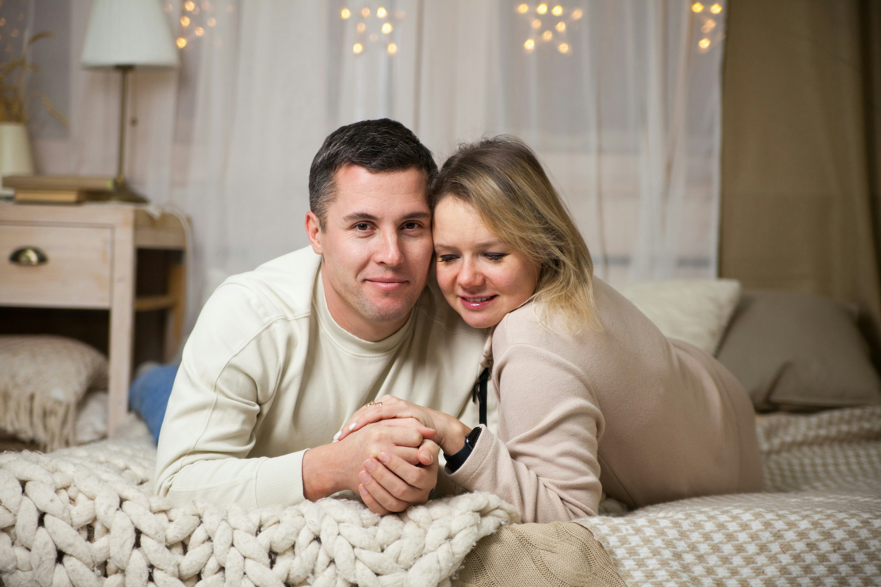 pregnant couple cuddling on bed at home in soft natural light