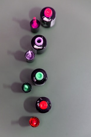 An artistic shot of nail polish bottles in bold colors lined up on a mirrored surface.