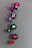 A series of open nail polish bottles are arranged in a diagonal line on a matte surface. The bottles have different shades of polish including pink, purple, green, and red. Shadows cast by the bottles are visible on the surface.