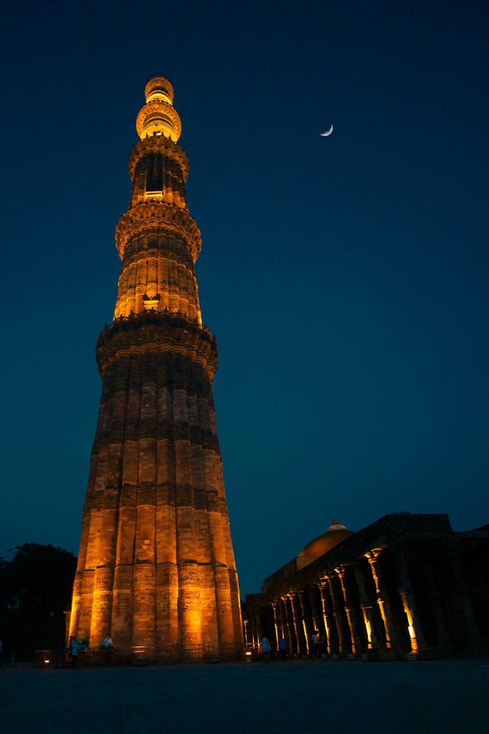 un'alta torre con luci di notte con Qutub Minar sullo sfondo