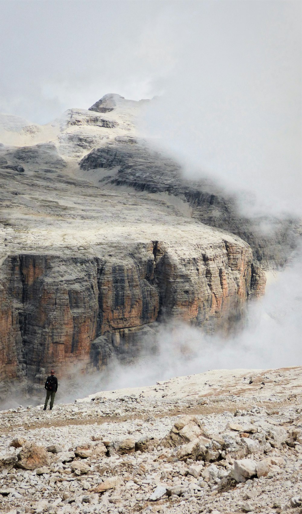 a person standing on a rocky hillside with a mountain in the background