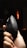 A hand is holding a black ergonomic mouse with perforations on the sides and a logo on the top. The background is dimly lit with an orange light source visible in the distance.