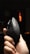 A hand is holding a black ergonomic mouse with perforations on the sides and a logo on the top. The background is dimly lit with an orange light source visible in the distance.