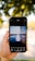 A hand is holding a smartphone displaying an image editing app. The app shows a photo of a building with reflective glass panels and the words 'Your only limit is your mind' overlaid on it. The background is out of focus, featuring greenery and dappled sunlight.