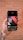 A hand is holding a smartphone displaying an image editing app. The screen shows a design with the text 'Think like an artist' in white on a dark background with red and black geometric shapes. The background features a blurred, rustic brick wall.