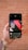 A hand is holding a smartphone displaying an image editing app. The screen shows a design with the text 'Think like an artist' in white on a dark background with red and black geometric shapes. The background features a blurred, rustic brick wall.