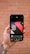 A hand is holding a smartphone displaying an image editing app. The screen shows a design with the text 'Think like an artist' in white on a dark background with red and black geometric shapes. The background features a blurred, rustic brick wall.