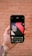 A hand is holding a smartphone displaying an image editing app. The screen shows a design with the text 'Think like an artist' in white on a dark background with red and black geometric shapes. The background features a blurred, rustic brick wall.
