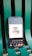 A smartphone displaying a digital art design with the phrase 'time is money' along with icons for currency and a timepiece. The phone is placed on a green metal chair or bench.