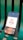 A smartphone displaying an app interface with a design that reads 'Time is Money' alongside a money bag icon. The phone is placed on a green, metal bench with visible slats.
