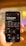 A hand is holding a smartphone displaying a screen with options for selecting the perfect layout for multiple platforms. The smartphone screen shows various platform options such as Instagram, Facebook, TikTok, and more. The background is blurred, focusing attention on the phone.