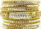 A stack of ornate bangles encrusted with sparkling gems. The bangles are layered with rows of white and brown stones, set against a rich gold background. The detailed craftsmanship and intricate patterns highlight their luxurious appearance.