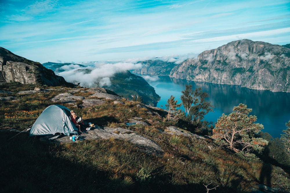 a person sitting on a rock by a tent and a body of water