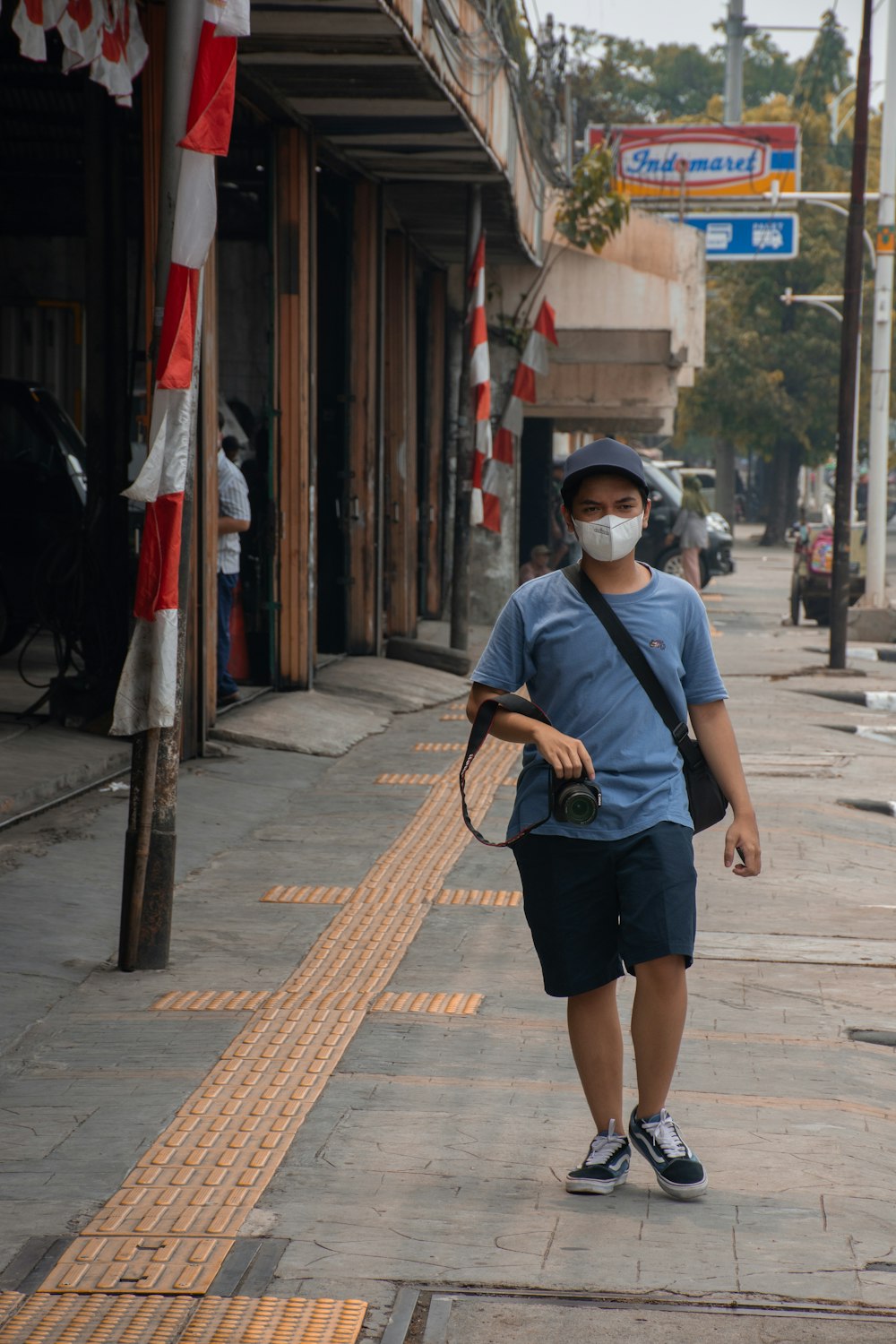 a person wearing a mask and a hat walking down a sidewalk