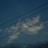 A sky with scattered white clouds and three prominent horizontal power lines intersecting the image. The clouds have varying textures and are illuminated against a blue-toned sky that transitions from lighter to darker shades.