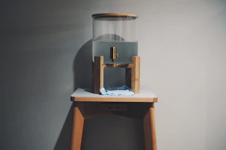 A clean water dispenser with a clear glass of water on a wooden table in a bright, modern office setting.