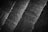 A black and white image of textured stone tiles arranged in diagonal lines. The texture is rough, with visible grain and patterns on the surface.