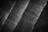 A black and white image of textured stone tiles arranged in diagonal lines. The texture is rough, with visible grain and patterns on the surface.