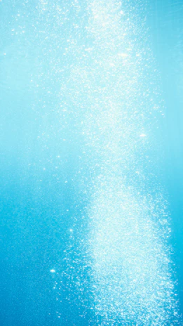 A diver ascending toward the surface with bubbles trailing behind against a backdrop of deep blue.