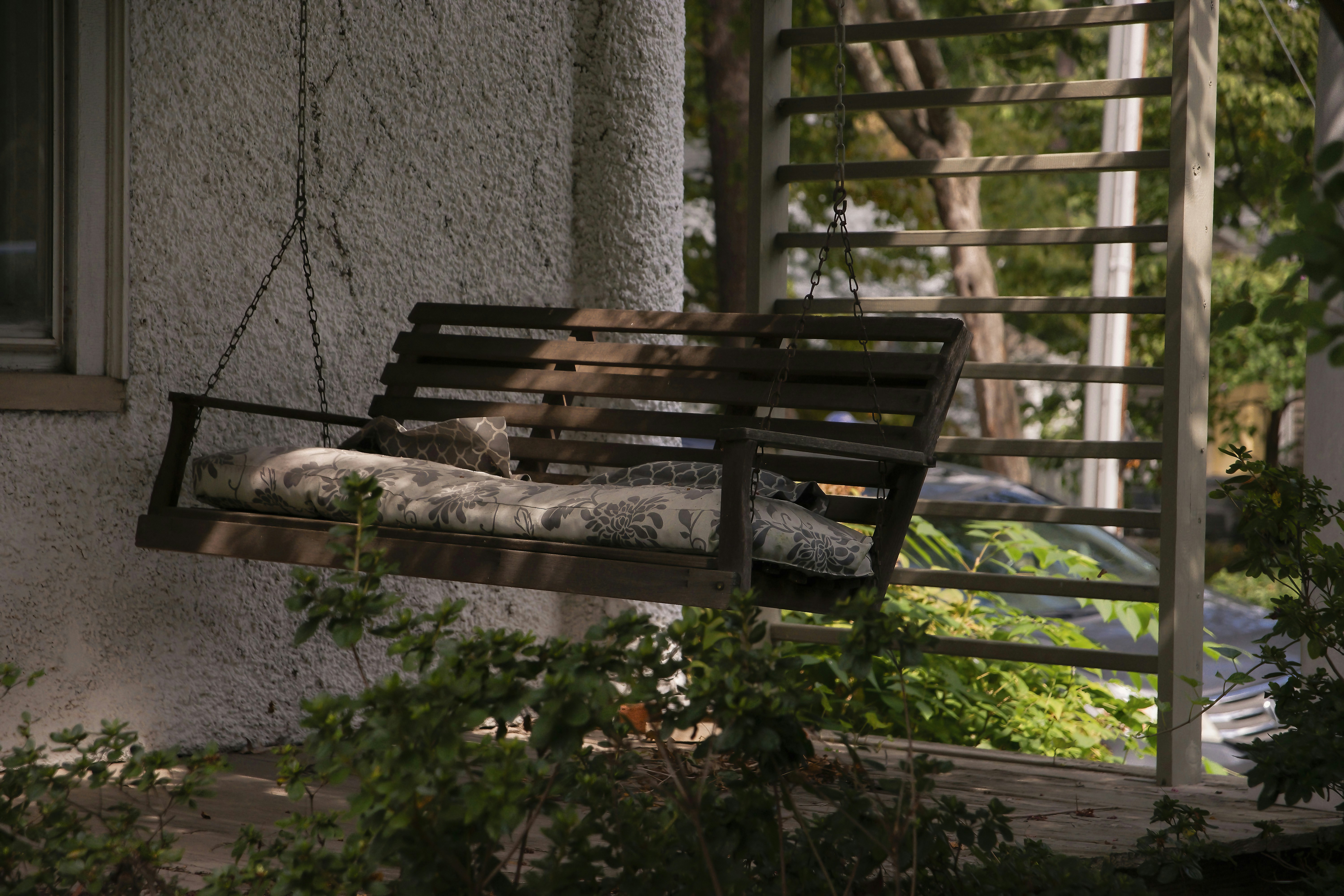 Old wooden porch swing seat in the shade, surrounded by green leaves.