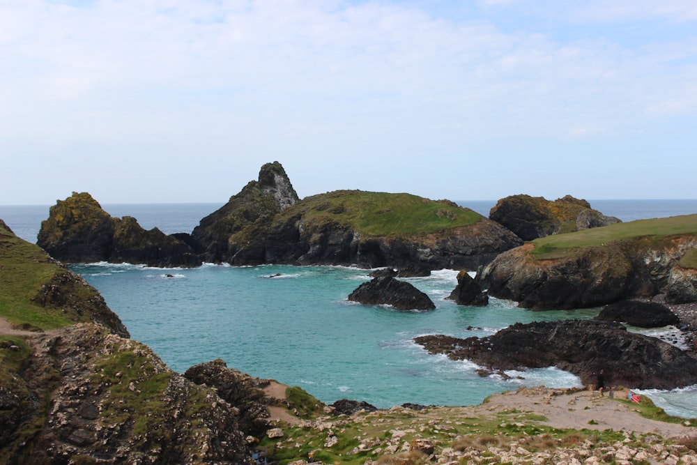 a rocky beach with a body of water and a large rock formation with Kynance Cove in the background