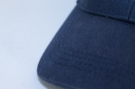 Hands inspecting the stitching detail on a brimix cap, emphasizing craftsmanship.