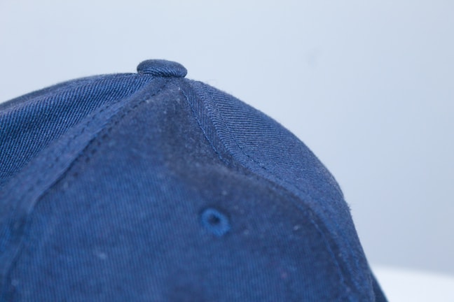 Close-up of a stylish black cap with royal blue accents on a wooden baseball bat background.