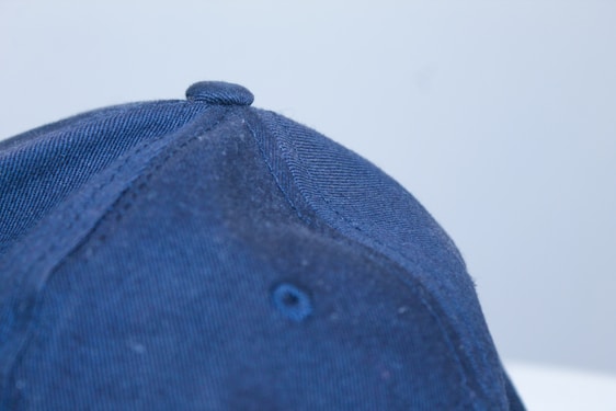 Close-up photo of a hand stitching a neutral-colored baseball cap in a bright, minimalist studio.