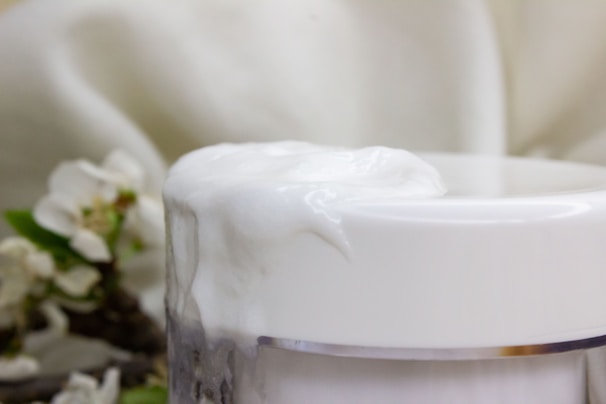 Close-up of a delicate cream jar surrounded by soft pastel flowers.