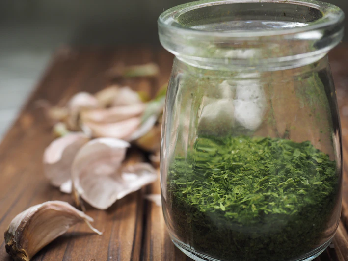 Close-up of a jar of chimi gel with fresh herbs around it on a rustic wooden table
