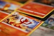 A close-up shot of various Pokémon trading cards laid out, with the focus on a Charmander card. The cards have vibrant and colorful illustrations featuring Pokémon characters and associated game stats.